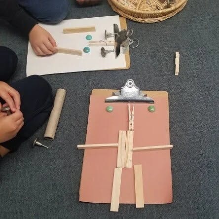 Child building a figure with wooden sticks on a clipboard