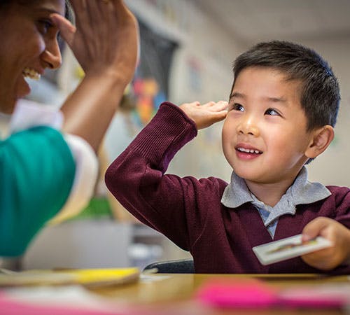 A person and a child giving each other a high five in a classroom