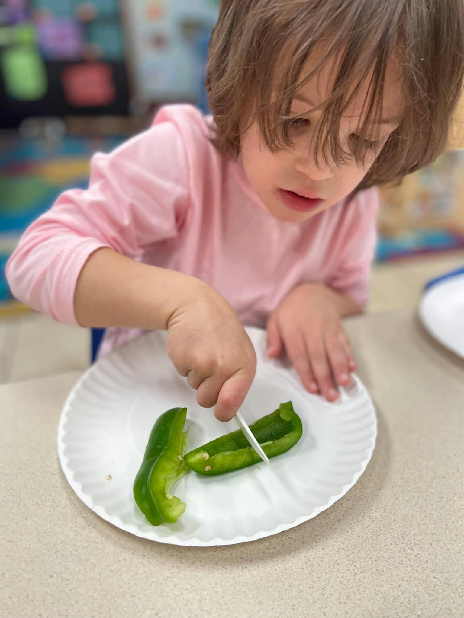 Child cutting green bell pepper on a paper plate