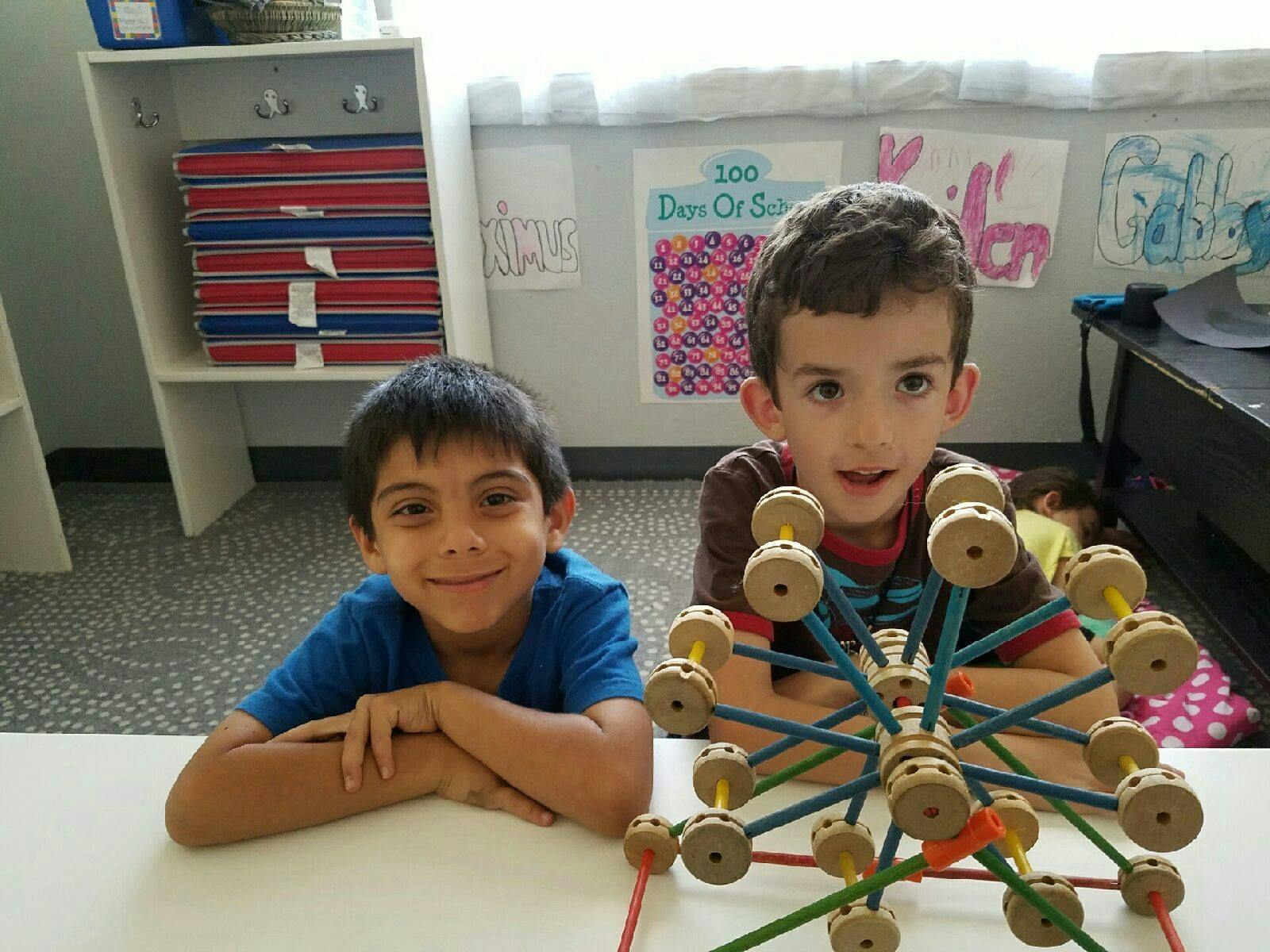Two children sitting at a table with a construction toy