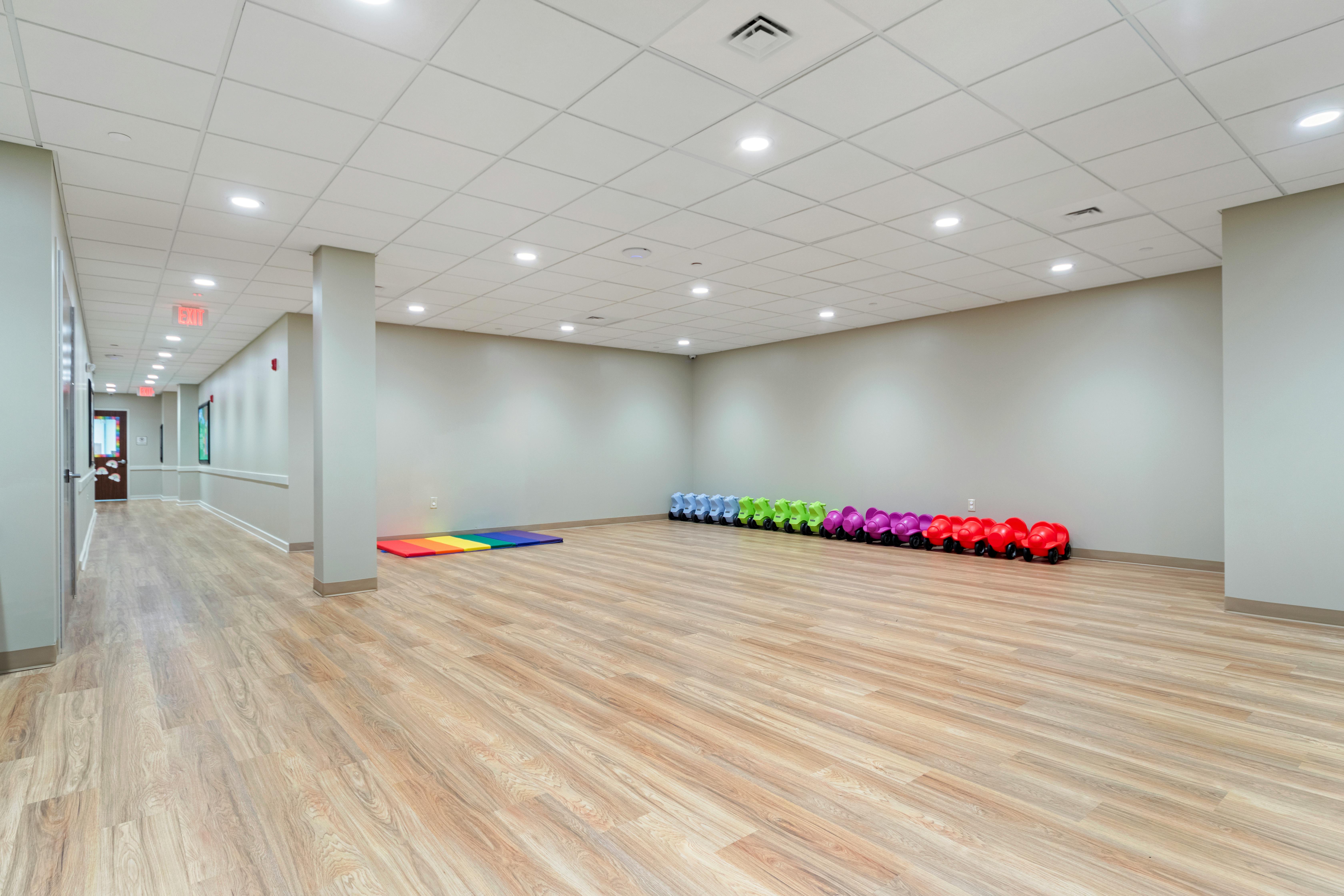 Empty activity room with colorful riding toys and a rainbow mat