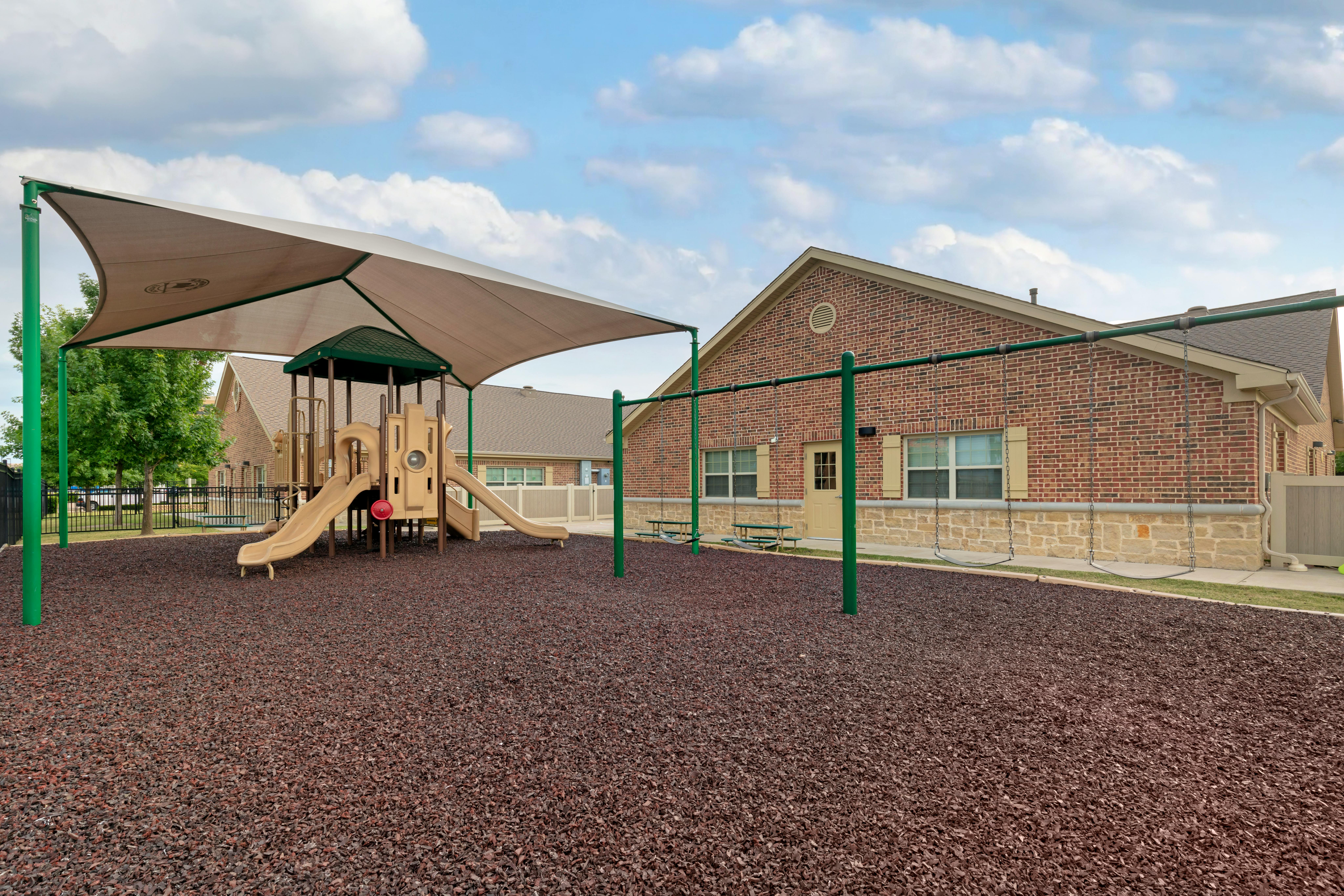 A beige playground structure with slides and a covered swing set on dark wood chips