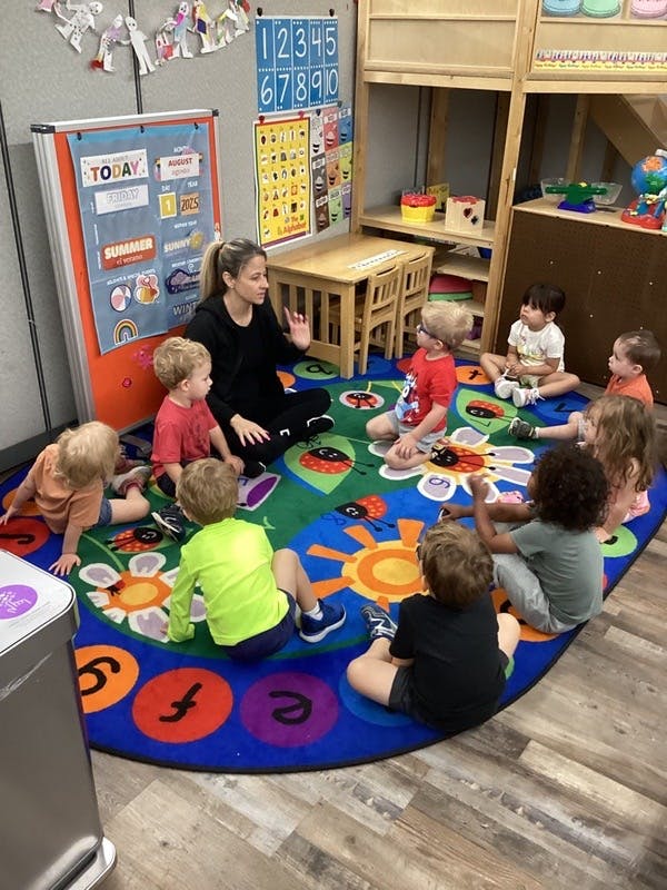 Adult and children sitting on a colorful rug in a classroom