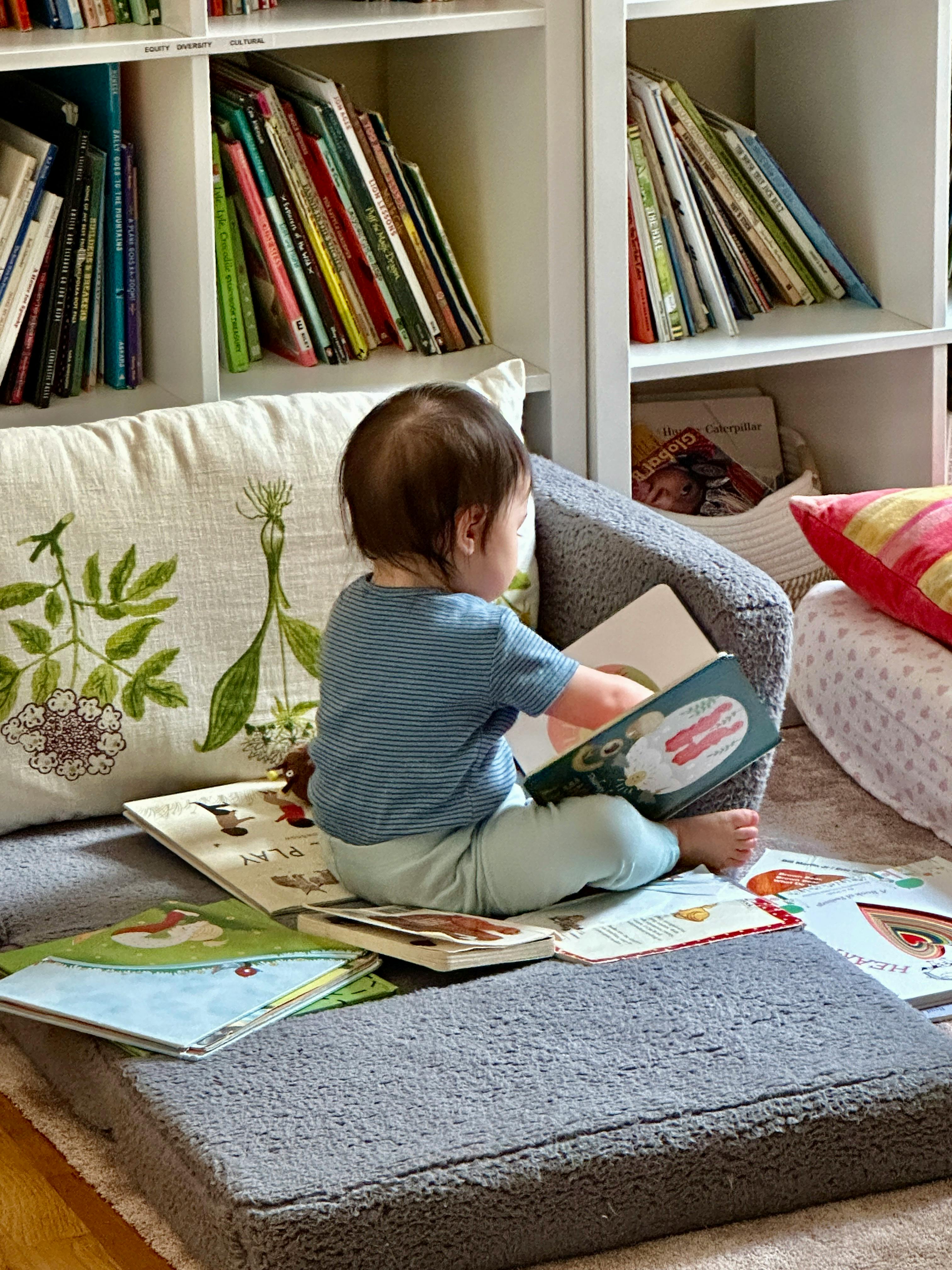 Child sitting on floor reading a book with bookshelves in background