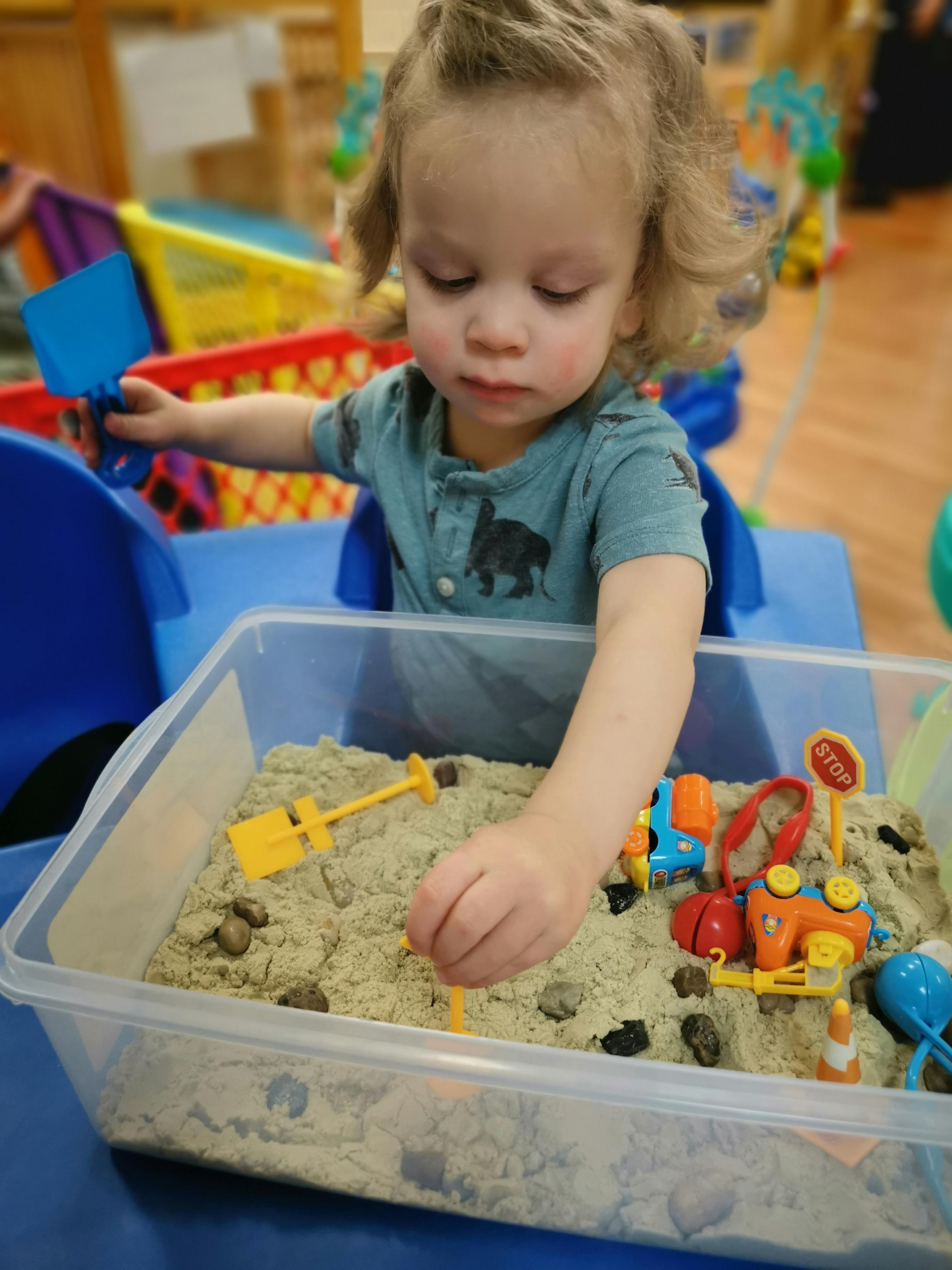 Child playing with sand and toys in a clear bin