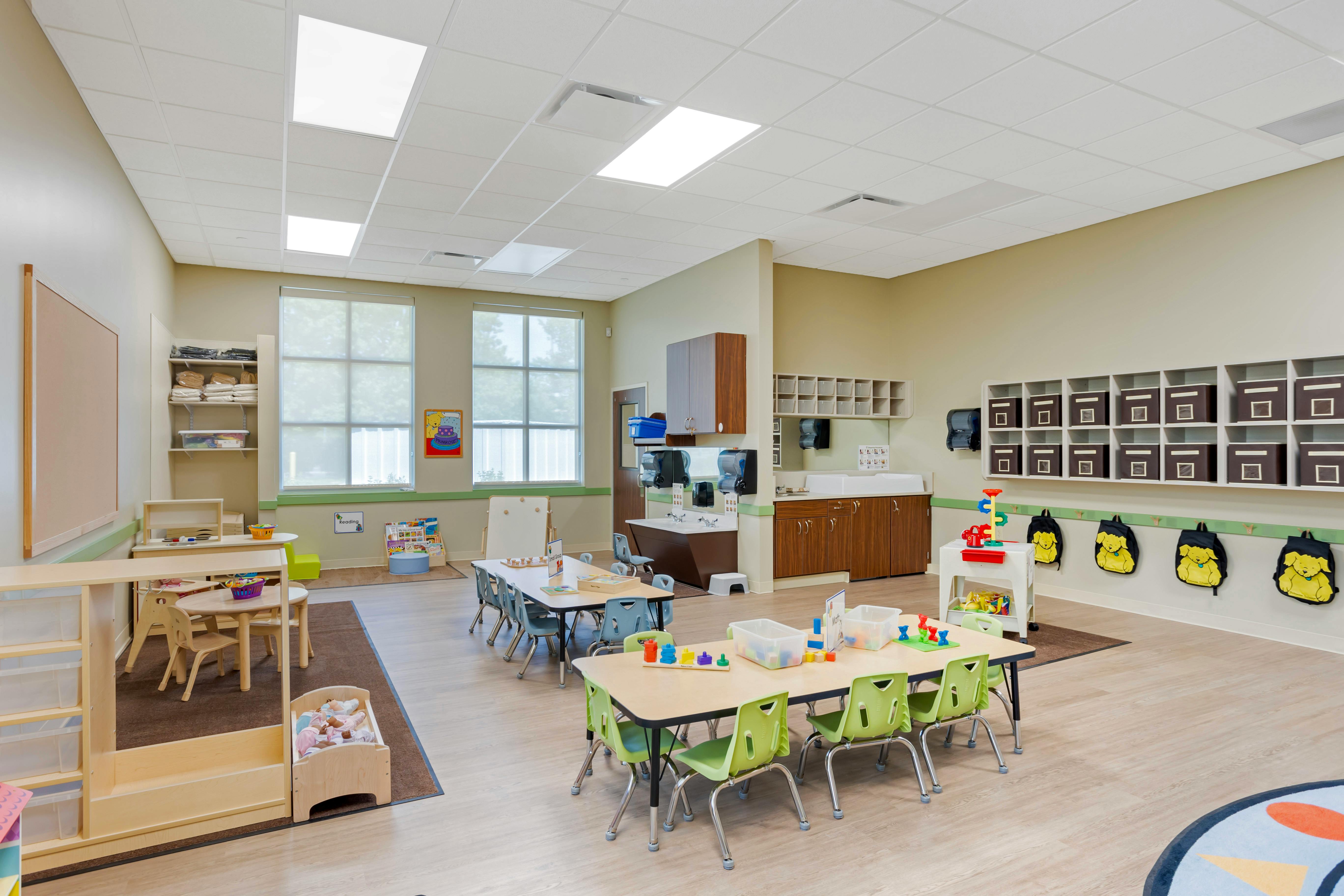 Classroom with child-sized tables and chairs, storage units, and sinks