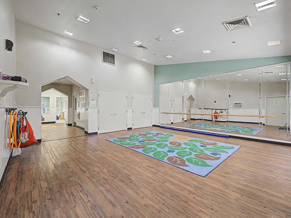 Empty dance studio with wood flooring and a large mirror with a ballet barre