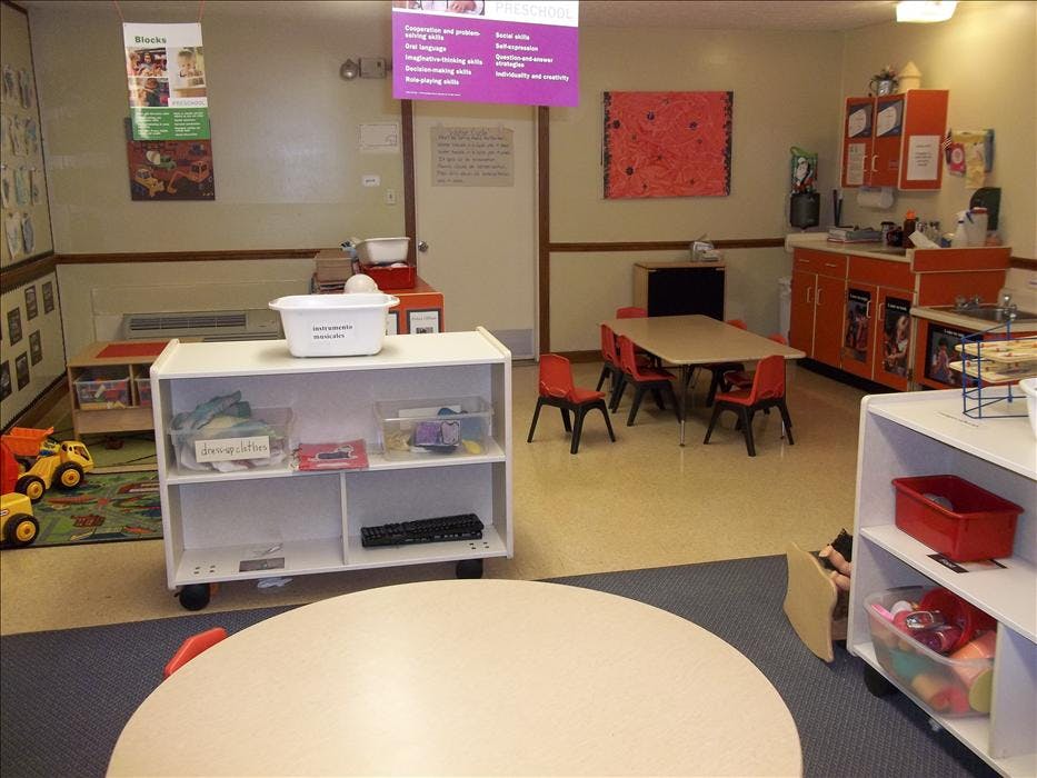Preschool classroom with play area, tables, chairs, and learning materials