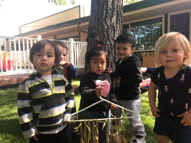 Five children standing outdoors, one holding a craft made from a hanger