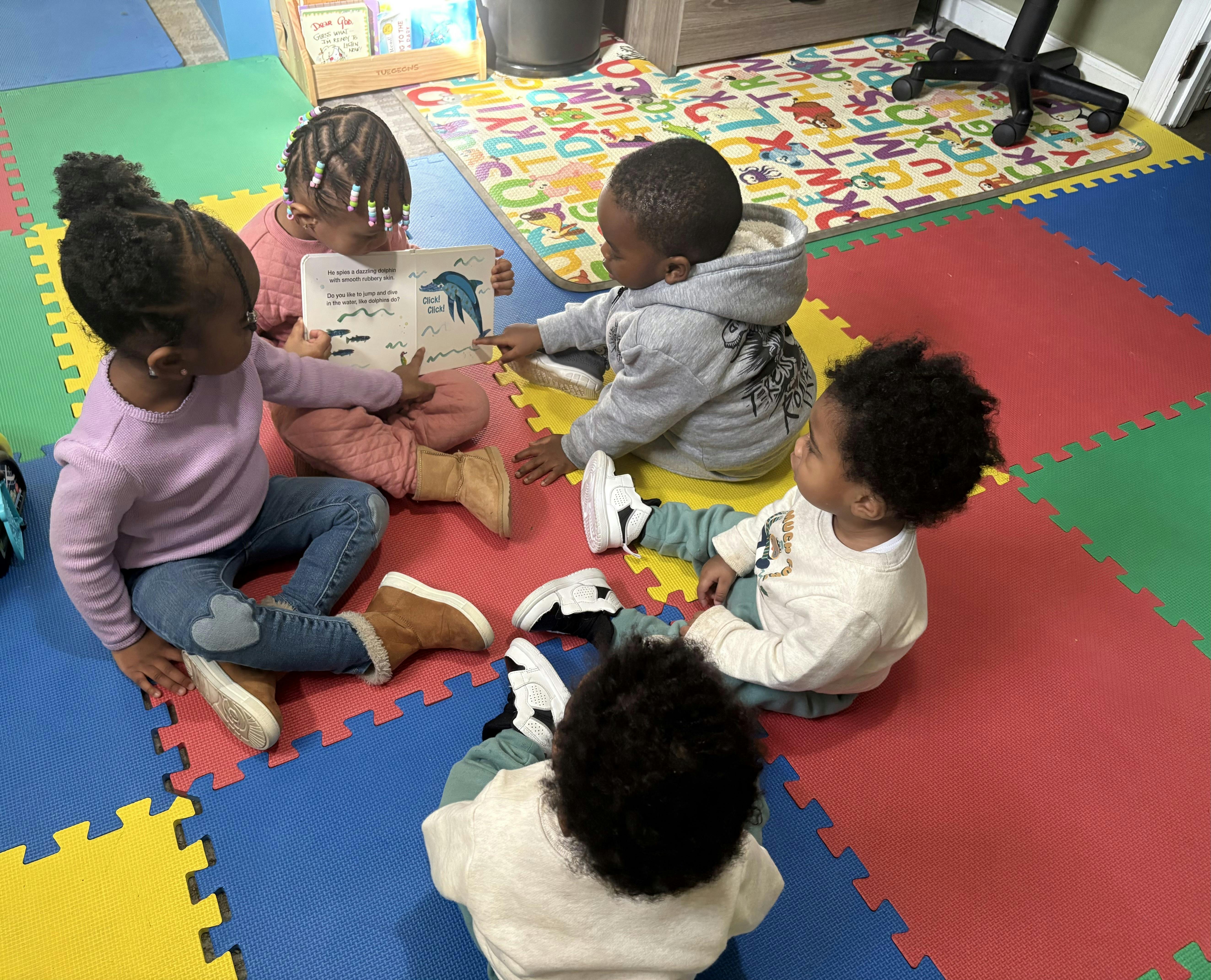Four children sitting on a colorful floor reading a book about dolphins