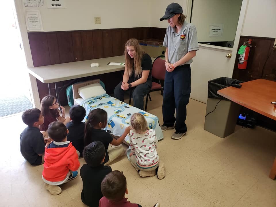 Two adults with a group of children gathered around a small bed