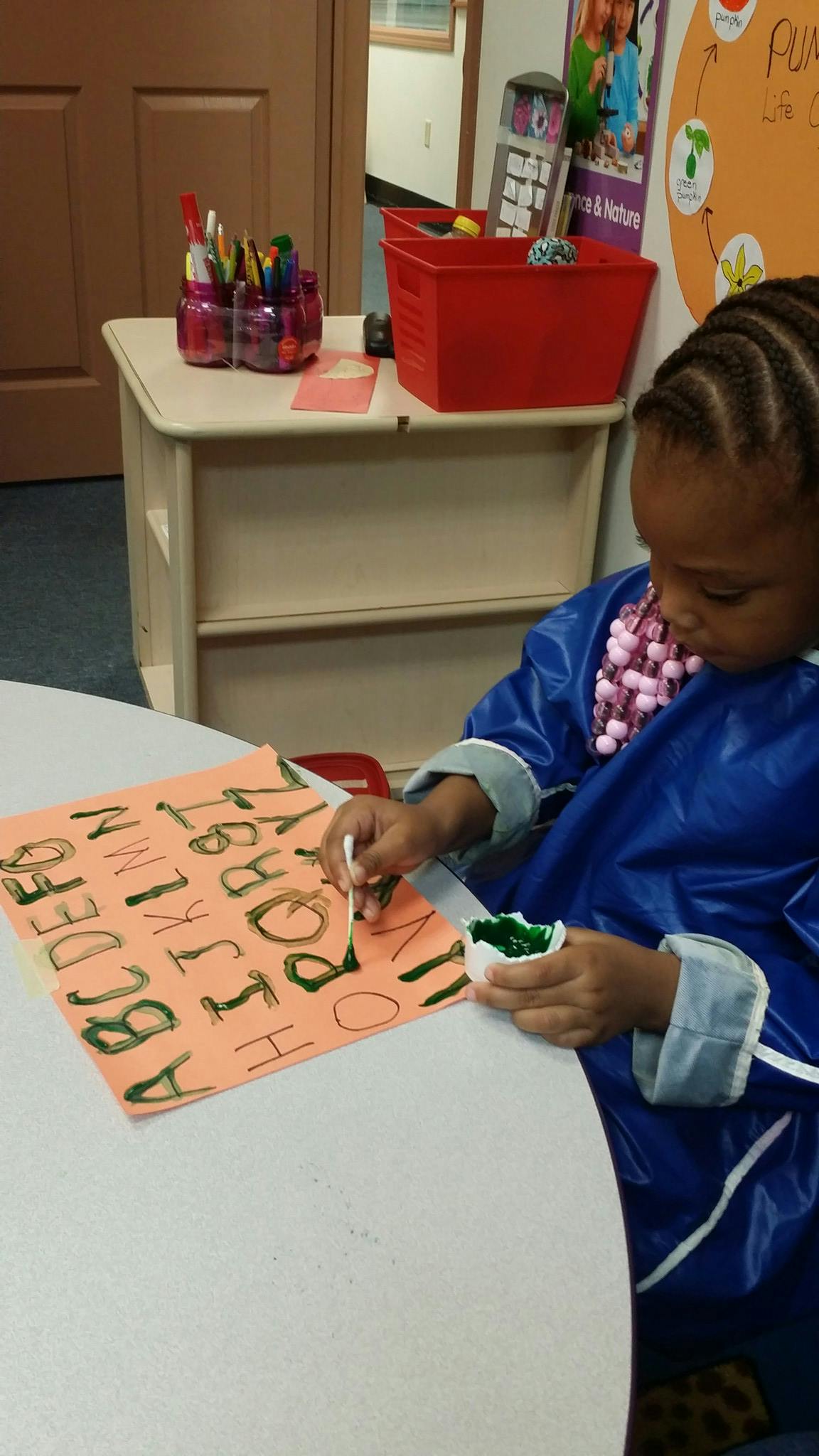 Child painting letters on a piece of paper in a classroom