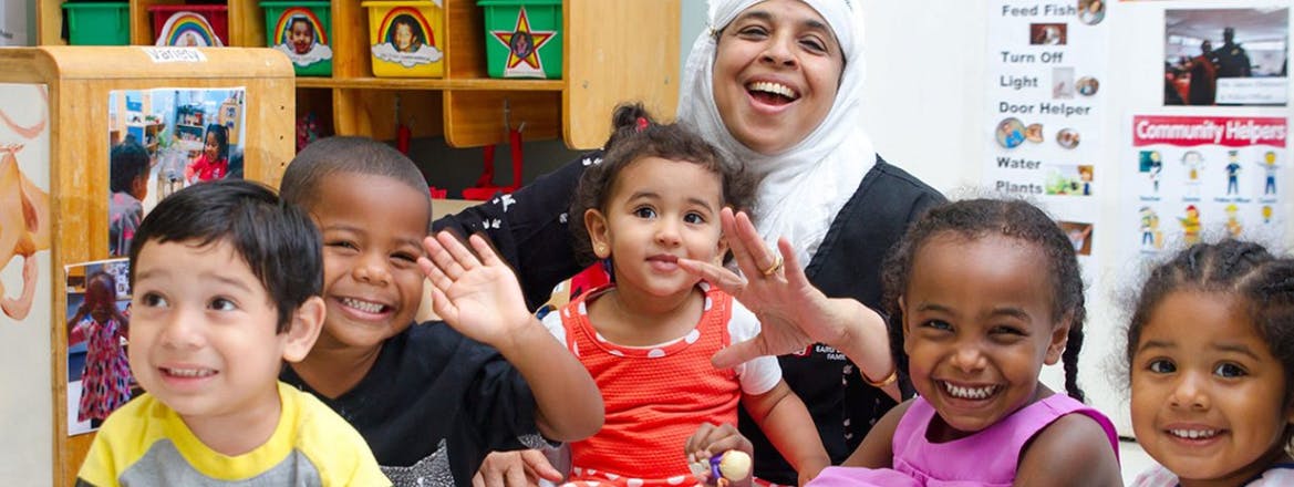 Adult and multiple children smiling and waving in a classroom
