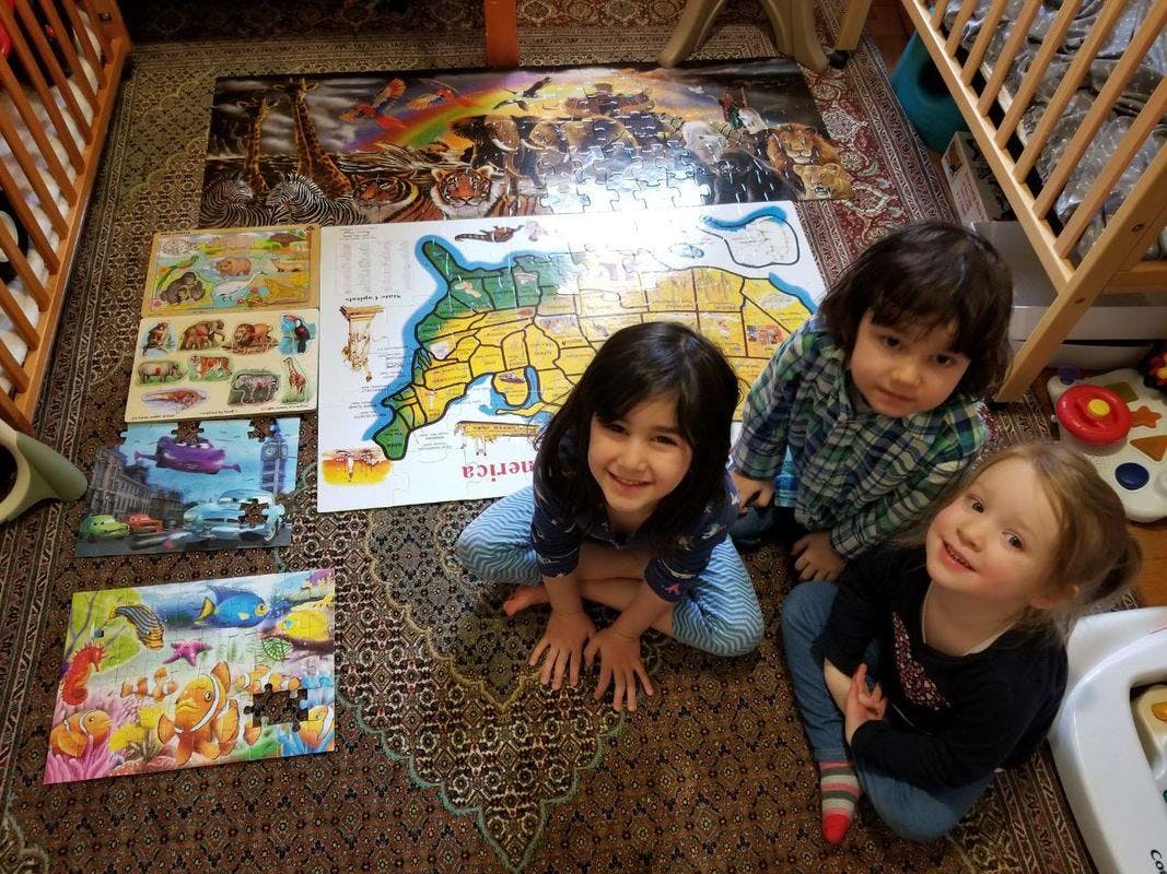 Three children on a rug with puzzles and a map