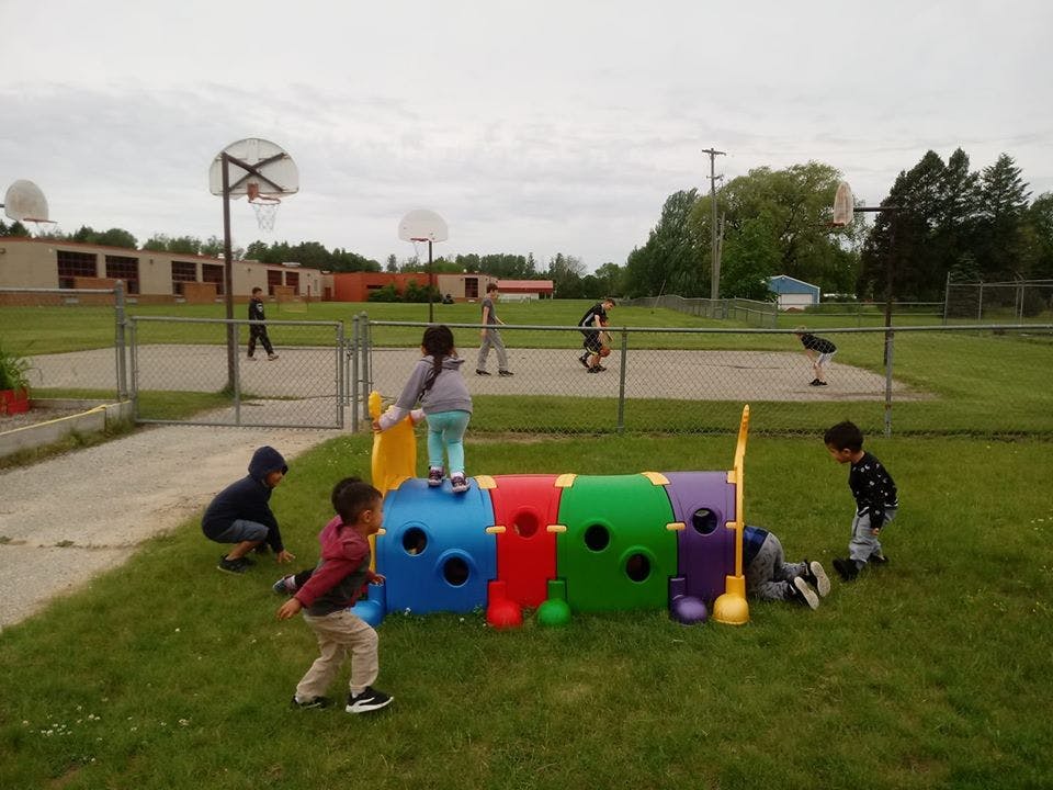 Children playing on a colorful caterpillar tunnel on a grassy playground