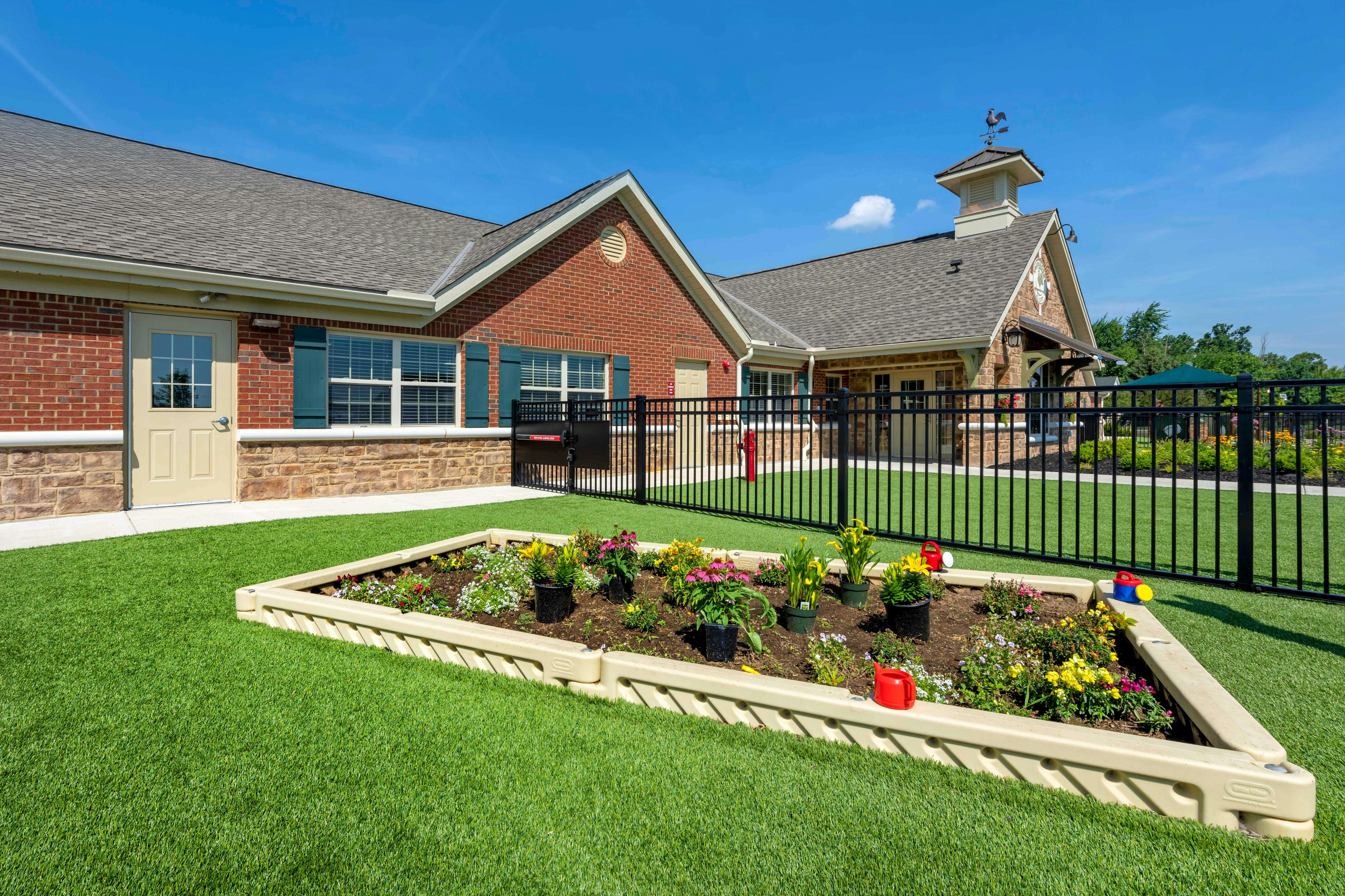 Children's garden beds with flowers on artificial grass next to a building