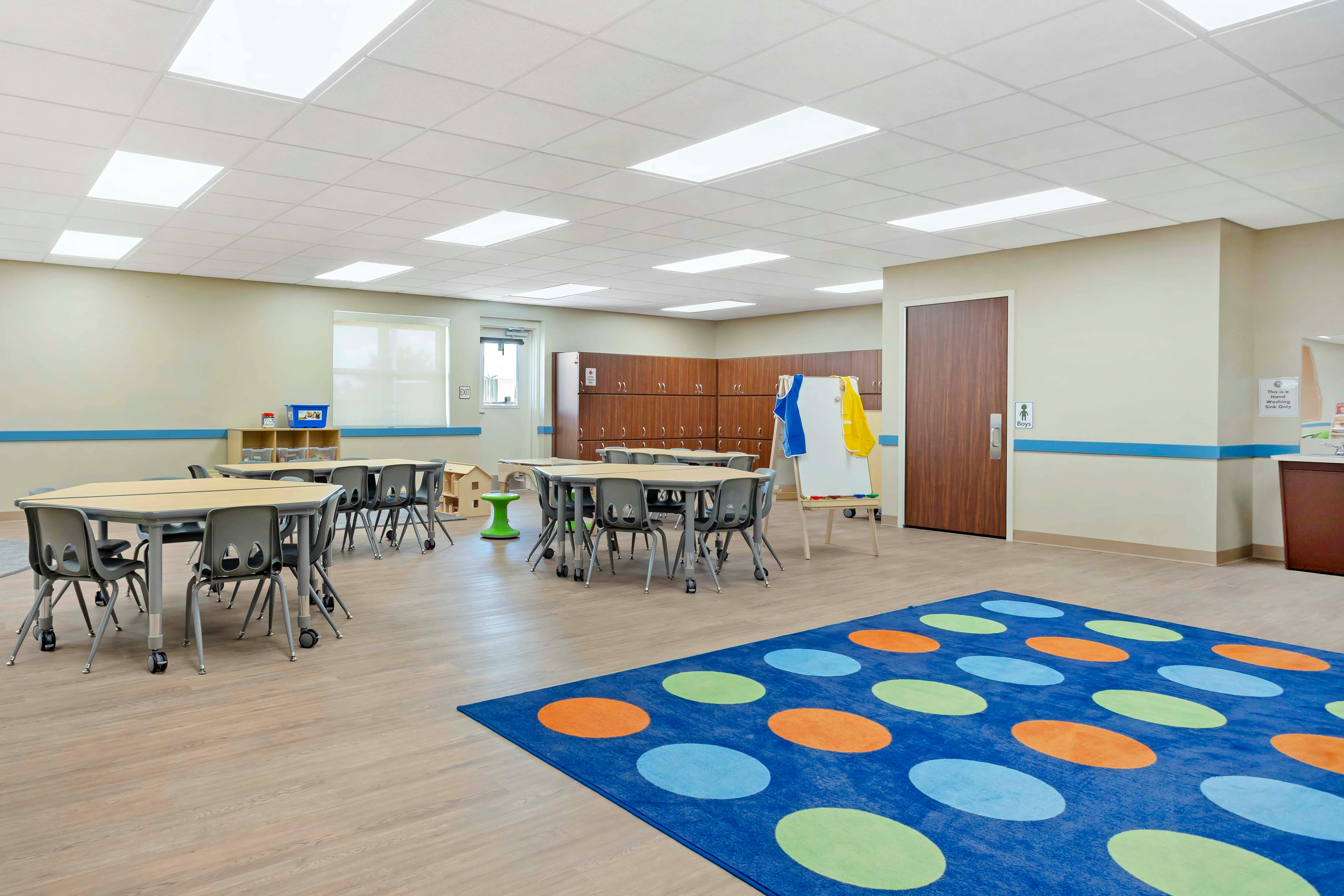 Empty classroom with small tables and chairs, lockers, and a colorful rug