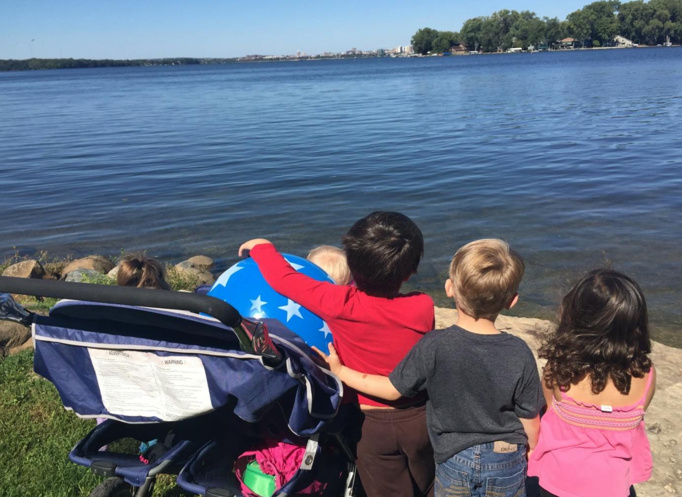 Three children and a baby in a stroller looking at a body of water