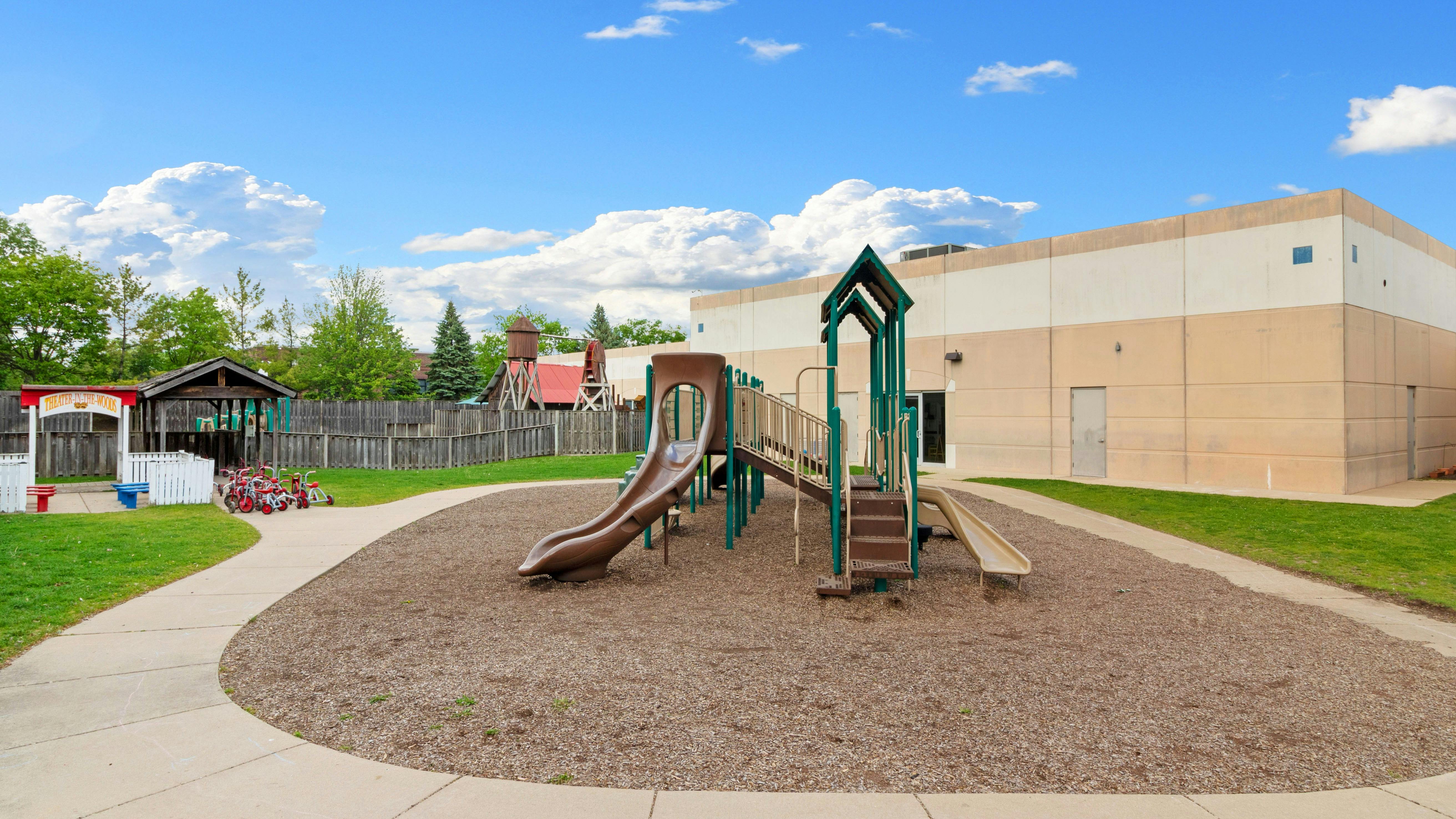 Playground with brown slides, green structures, wood chips, and a building