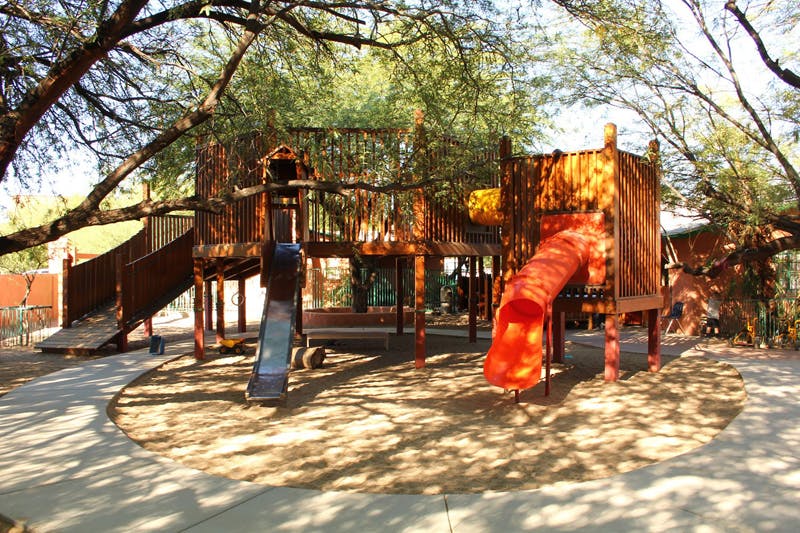 Wooden playground structure with slides under trees