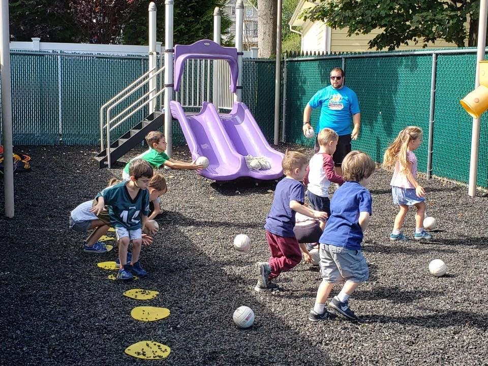 Children playing with balls on a playground with a person standing nearby