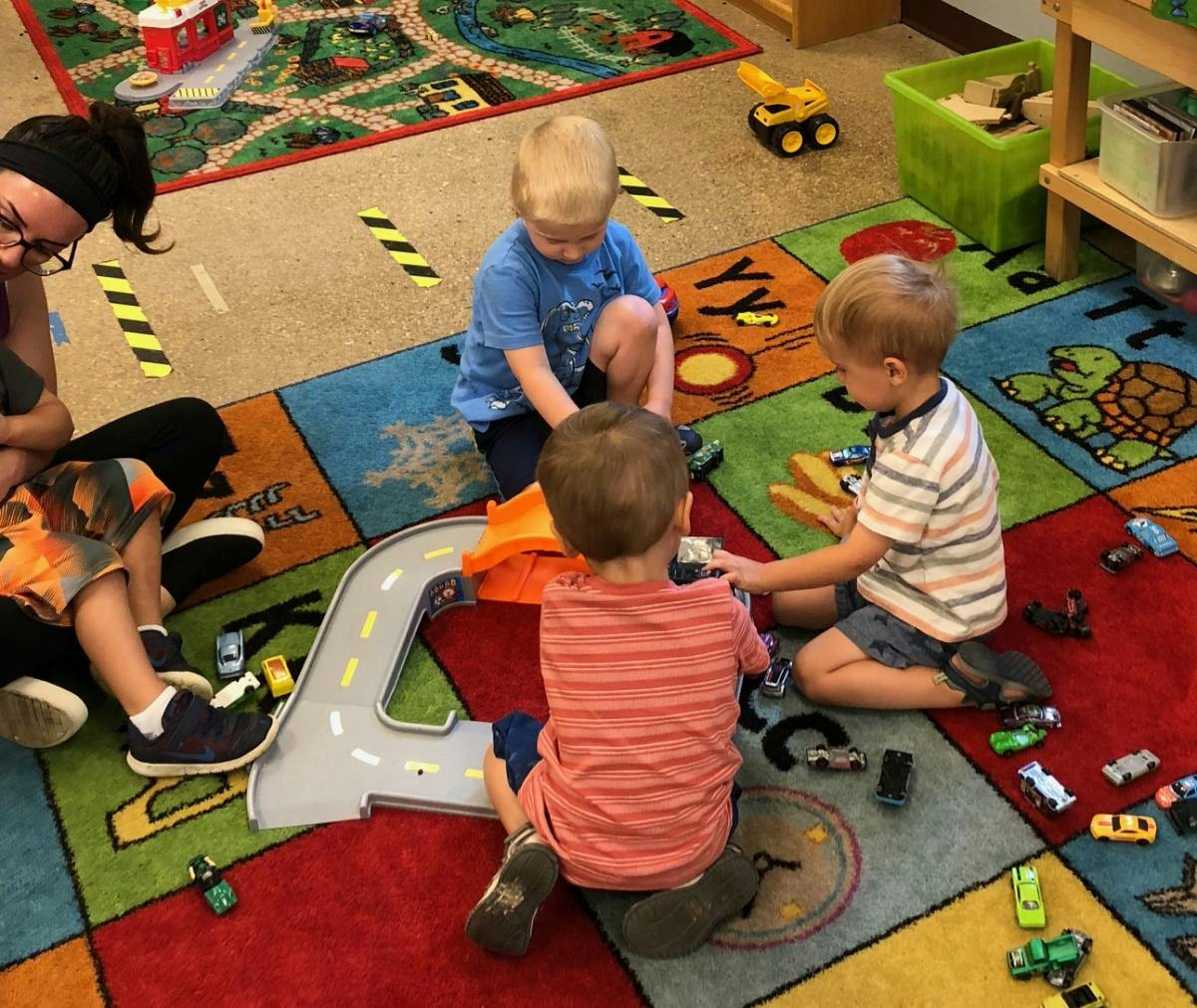 Adult and three children playing with toy cars on a colorful rug