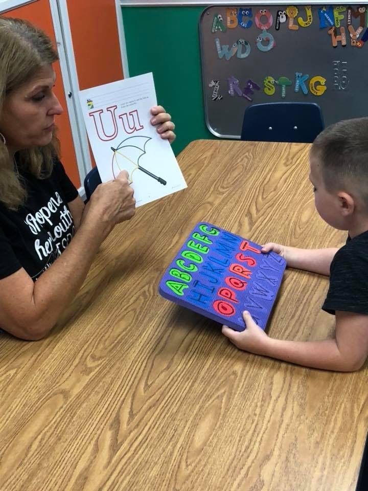 Person holding a letter U card and a child holding an alphabet puzzle