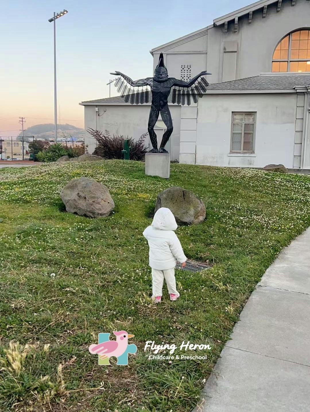 Child in white jacket walking on grass toward a statue