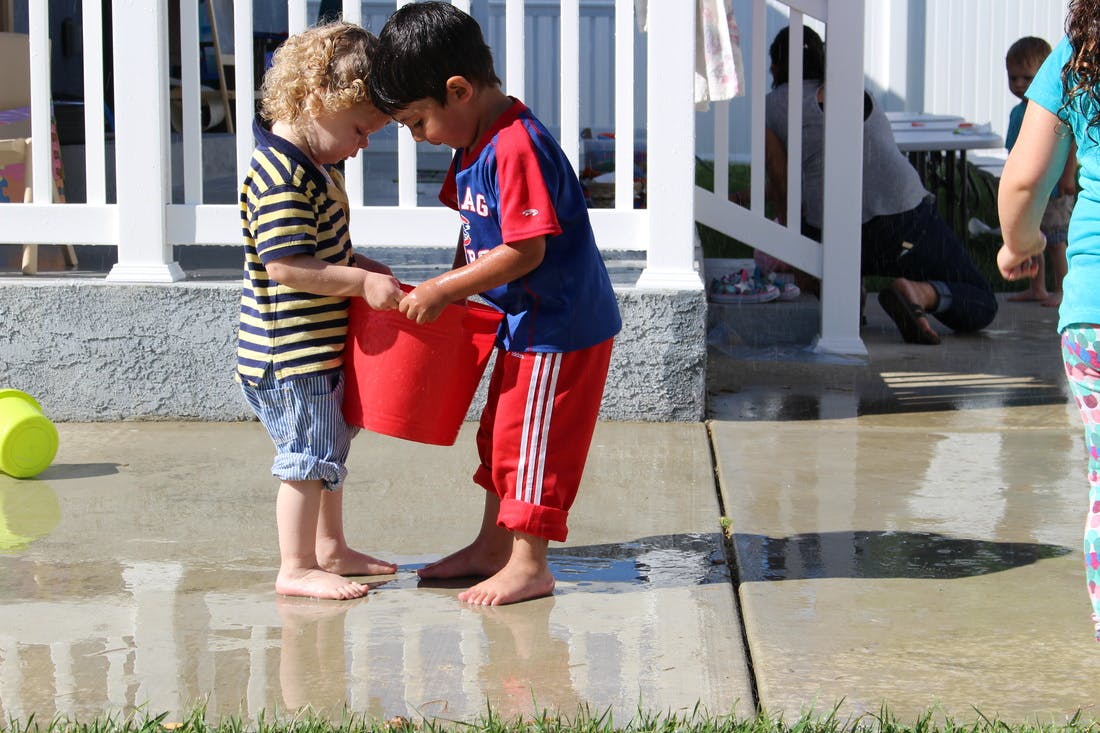 Two children holding a red bucket together on a wet surface