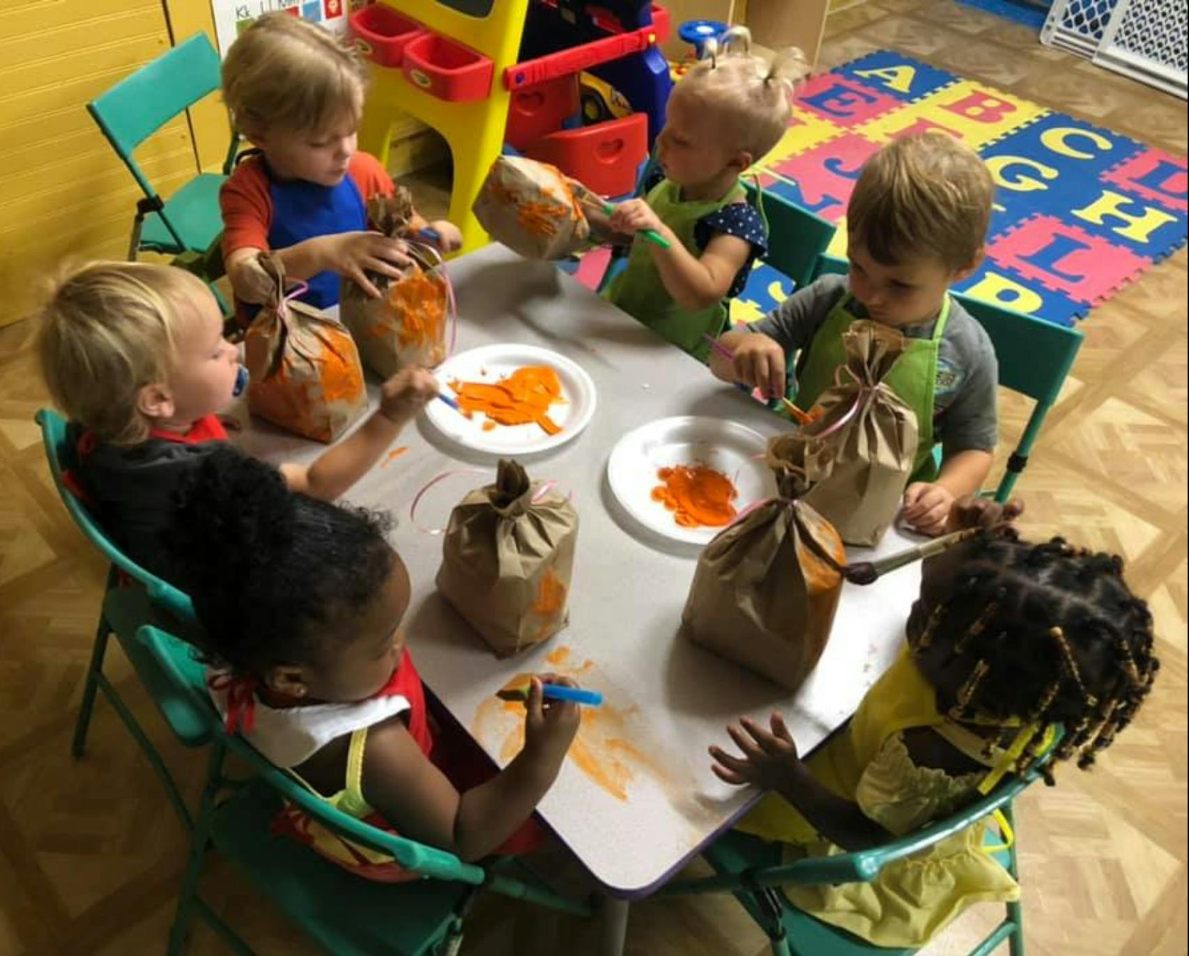 Children painting paper bags at a table