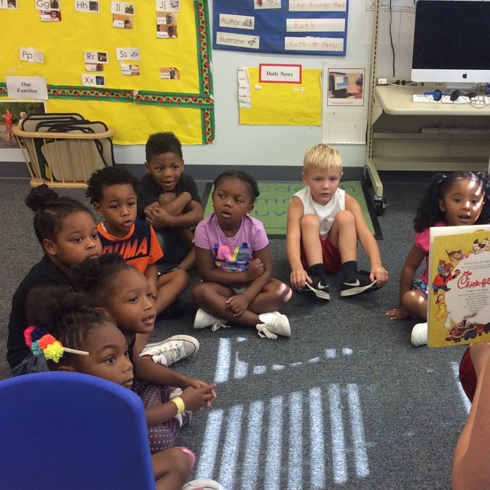Group of children sitting on the floor listening to a person read a book