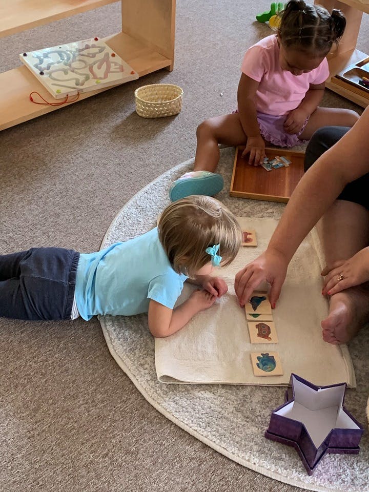 Two children and an adult playing with wooden blocks on a rug