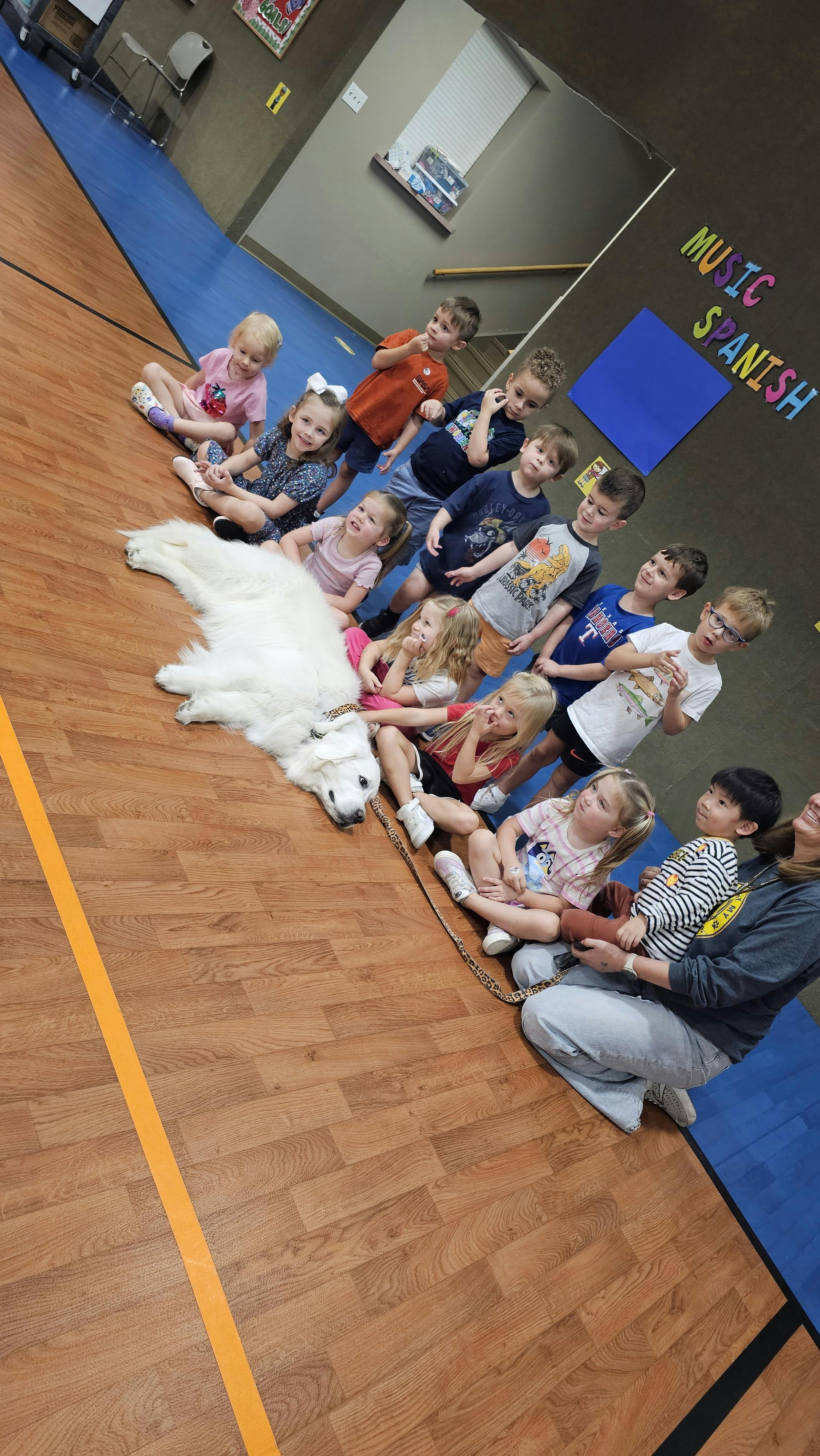 Children sitting on the floor with a large white dog and an adult