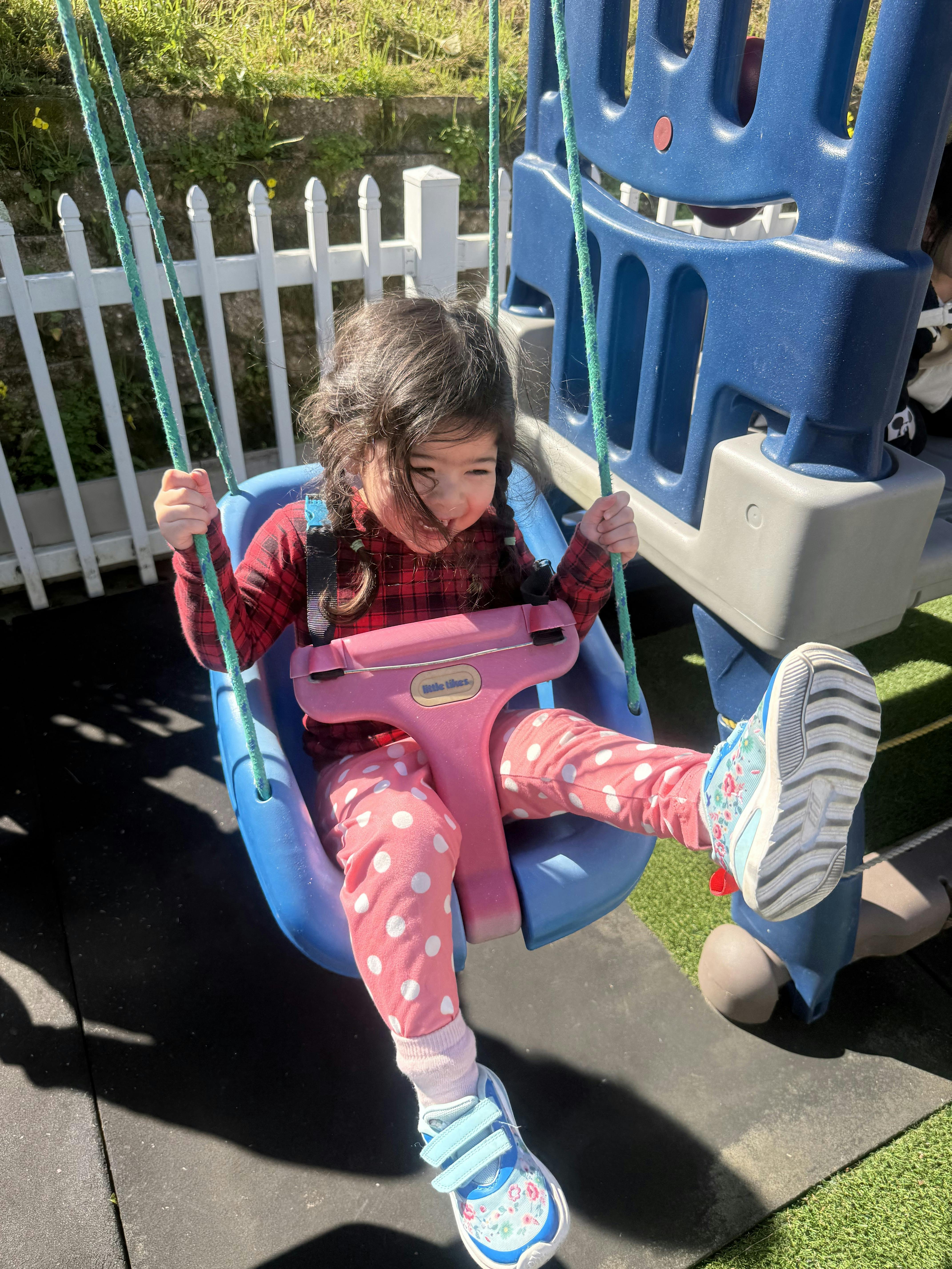 Child in a red shirt and polka dot pants sitting in a swing at a playground