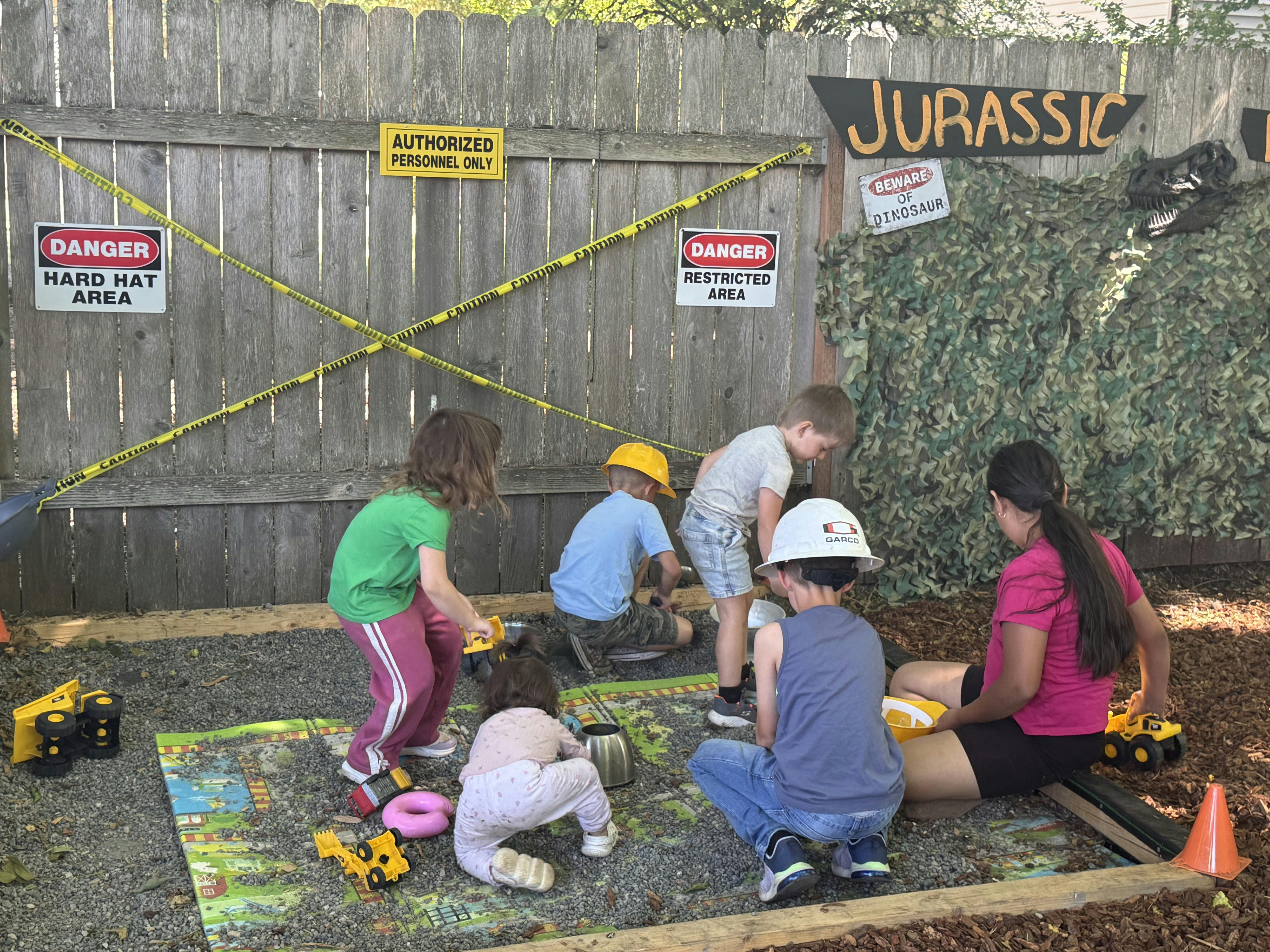 Group of children playing with toy trucks in a Jurassic-themed gravel pit
