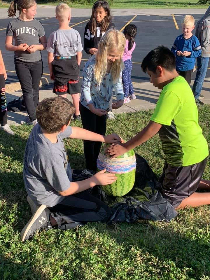 Children gathered around a watermelon wrapped in rubber bands