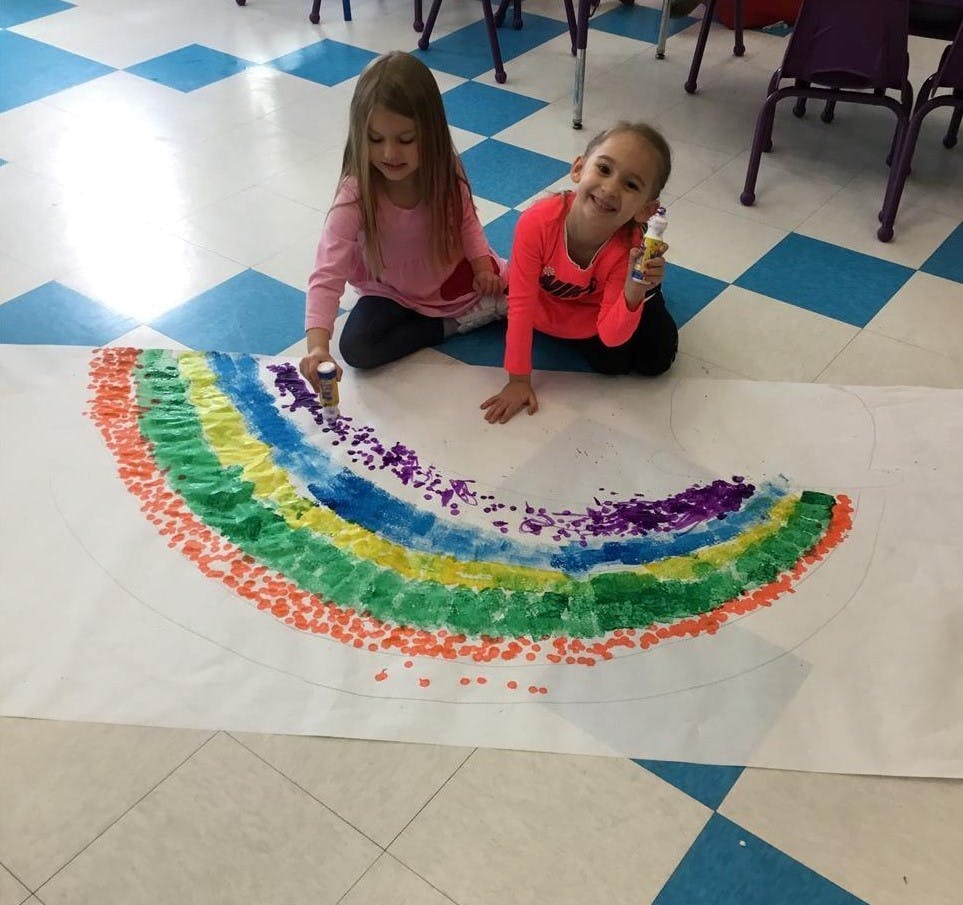 Two children kneeling on the floor making a rainbow craft
