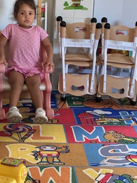 Child sitting on a pink chair on a colorful alphabet rug