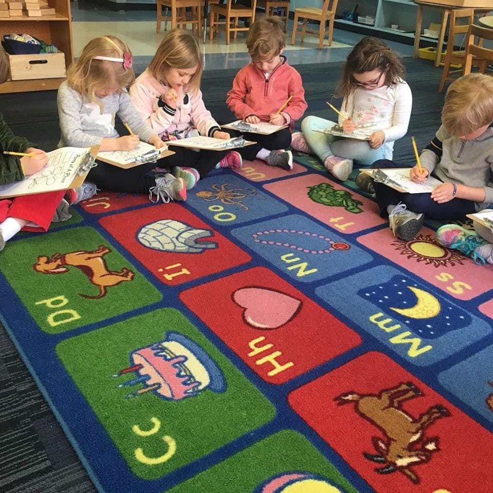Children sitting on a rug and writing on clipboards