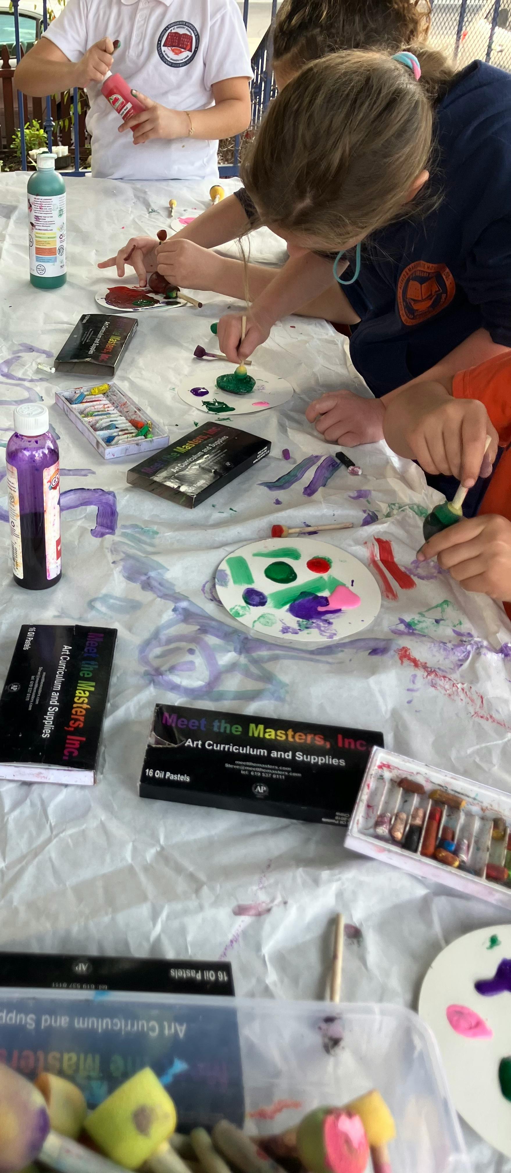 Children painting at a table covered in white paper with art supplies
