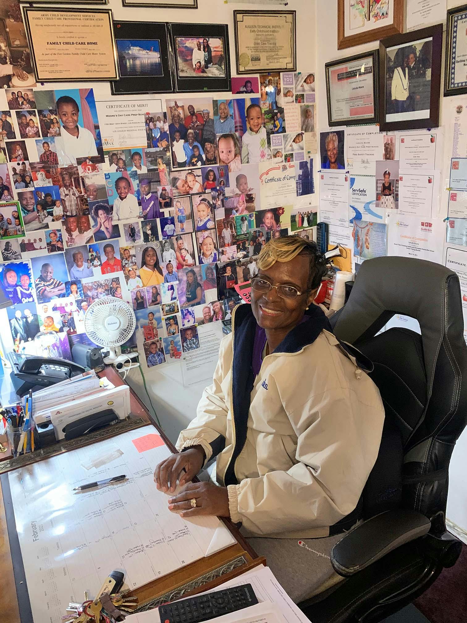 Person seated at a desk with a calendar, surrounded by photos and certificates