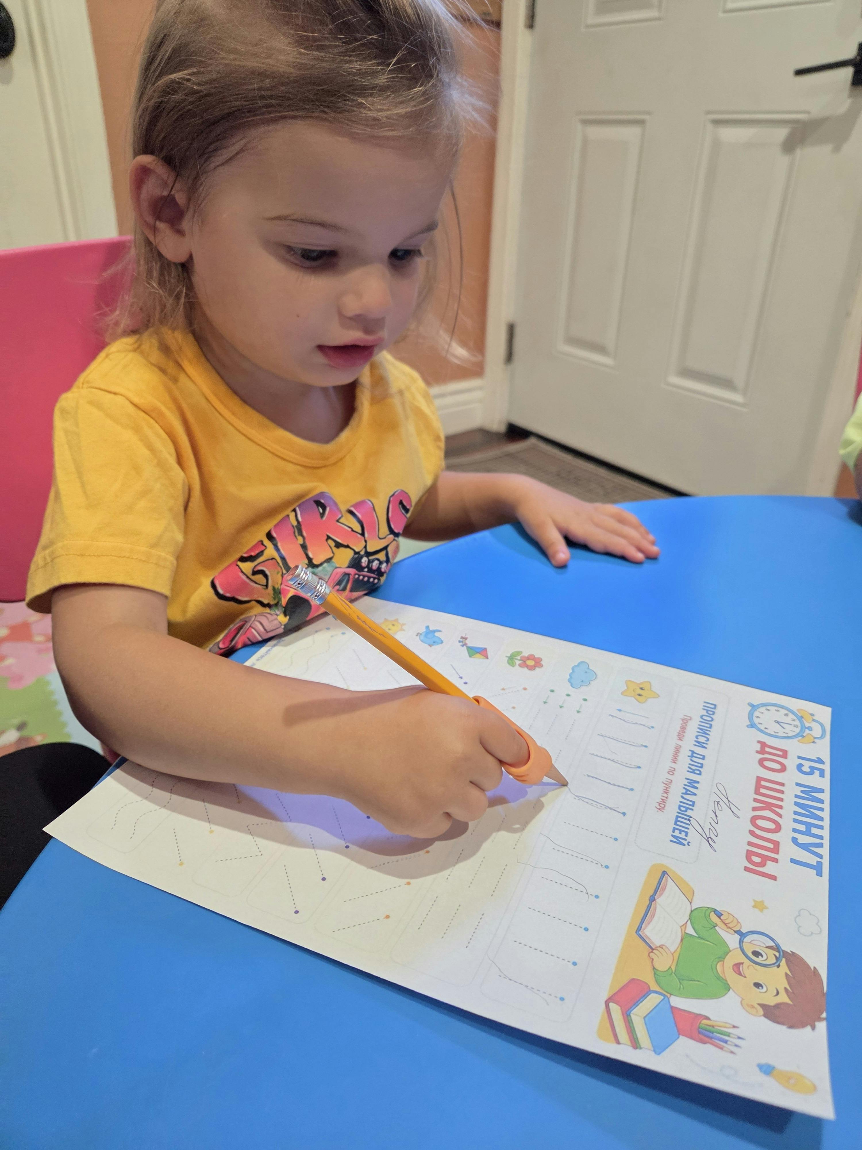 Child in yellow shirt tracing lines on a paper with a pencil