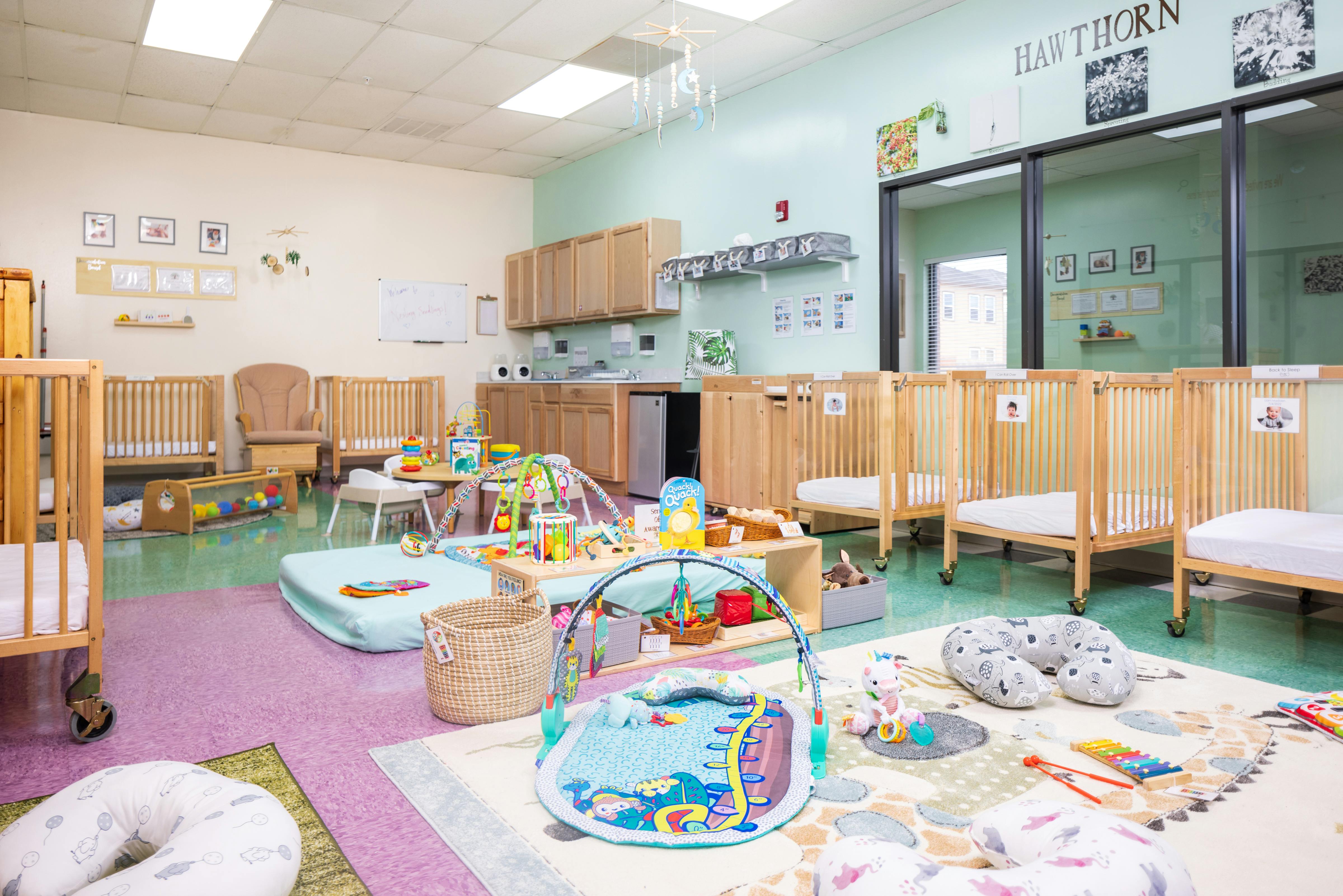 Infant classroom with cribs, play mats, and toys