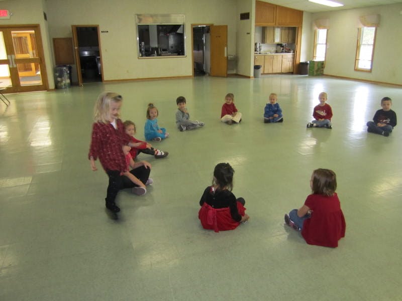 Children sitting in a circle on the floor, one child standing in the middle