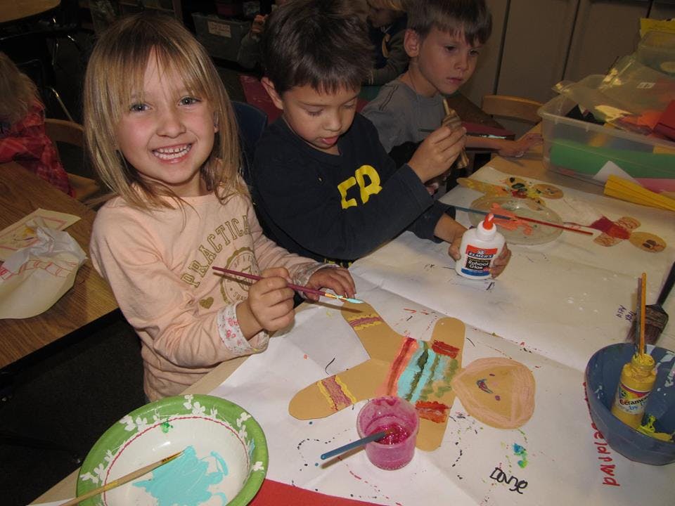 Three children painting and gluing crafts at a table