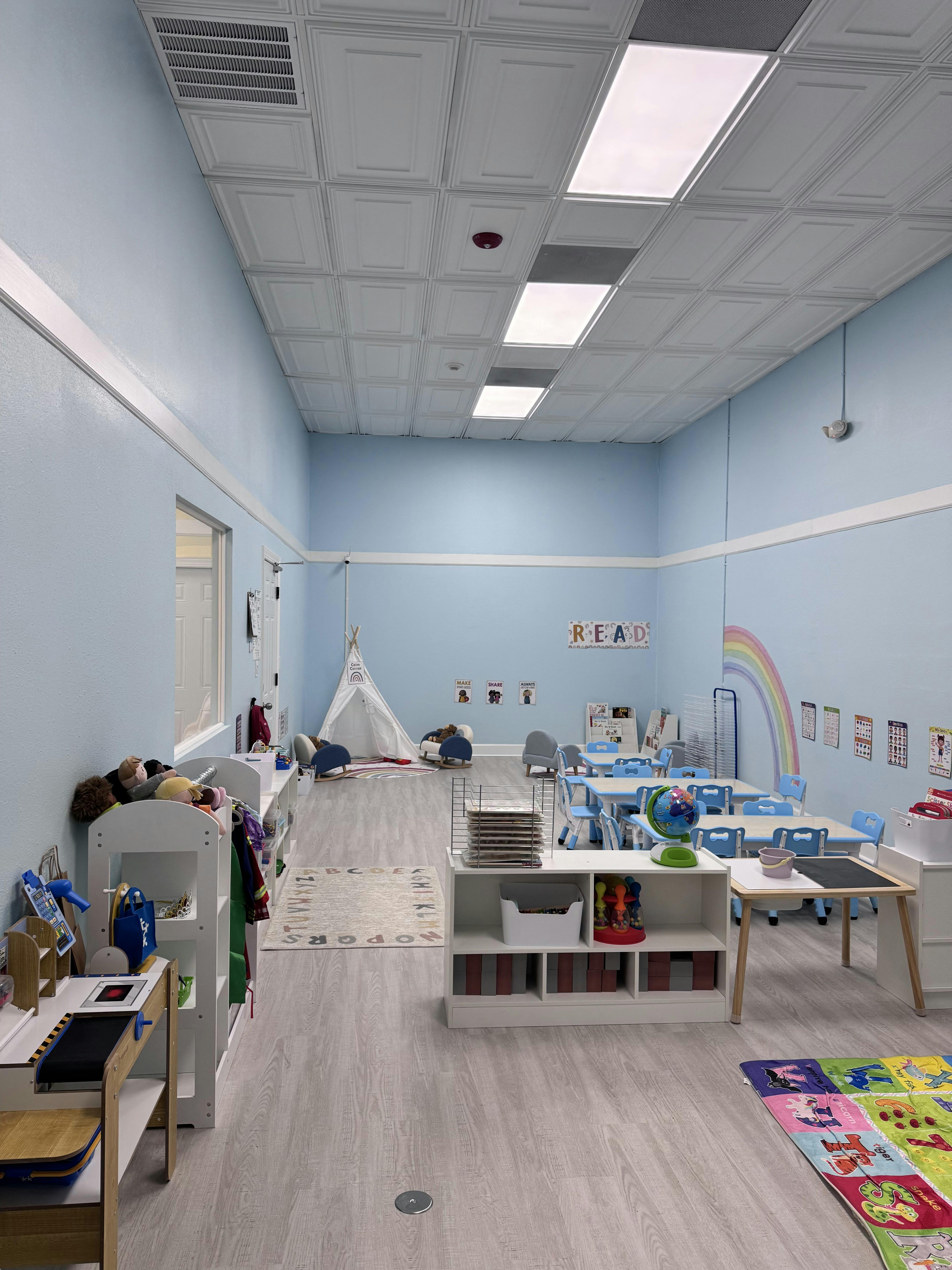 Classroom with small tables and chairs, a teepee, and a rainbow mural