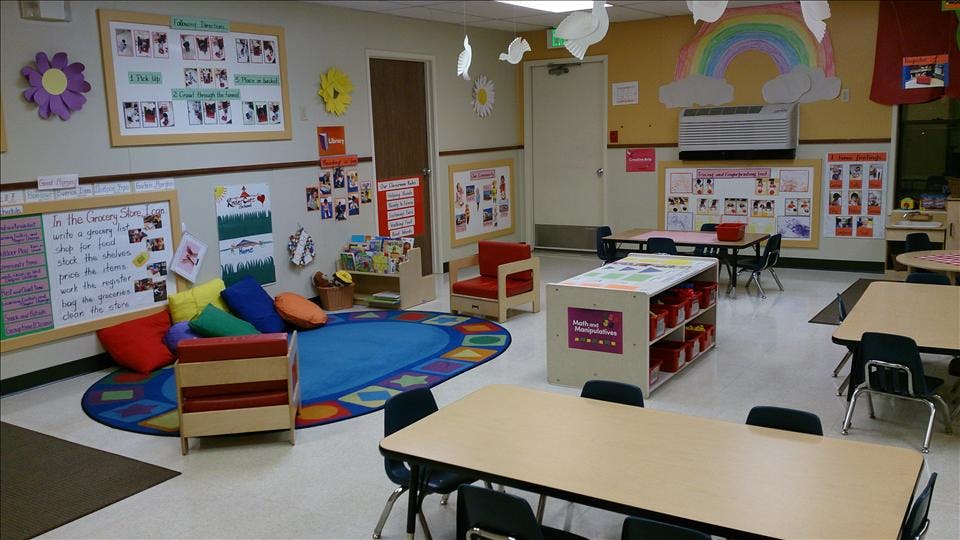 An empty classroom with tables, chairs, a reading nook with pillows, and decorations