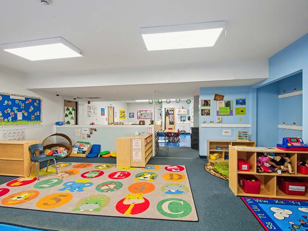 A colorful classroom with educational rugs and shelves filled with toys
