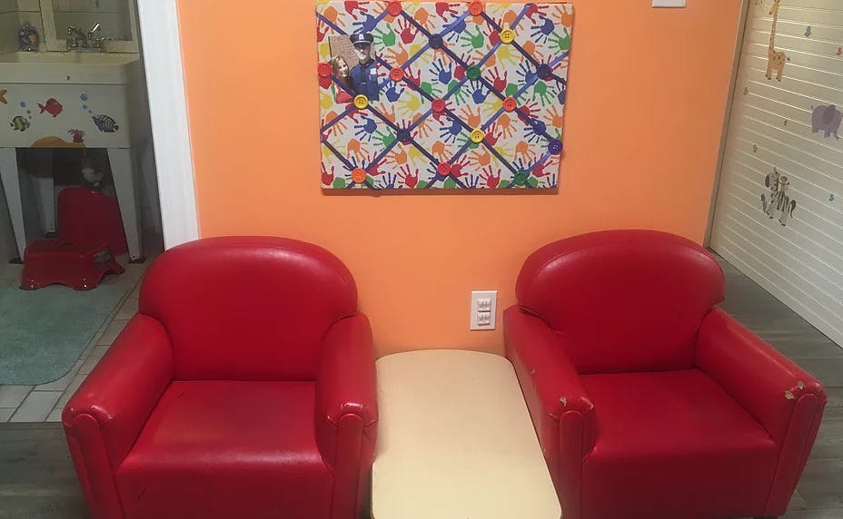 Two red chairs with a small table between them, colorful artwork on the wall