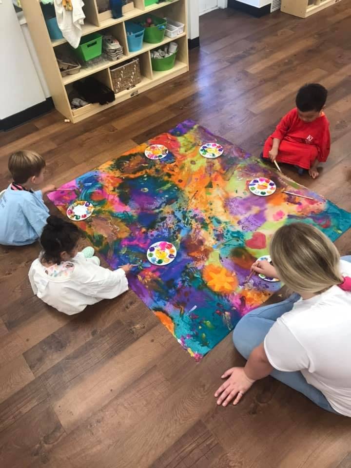 Adult and children painting on a large colorful canvas on the floor
